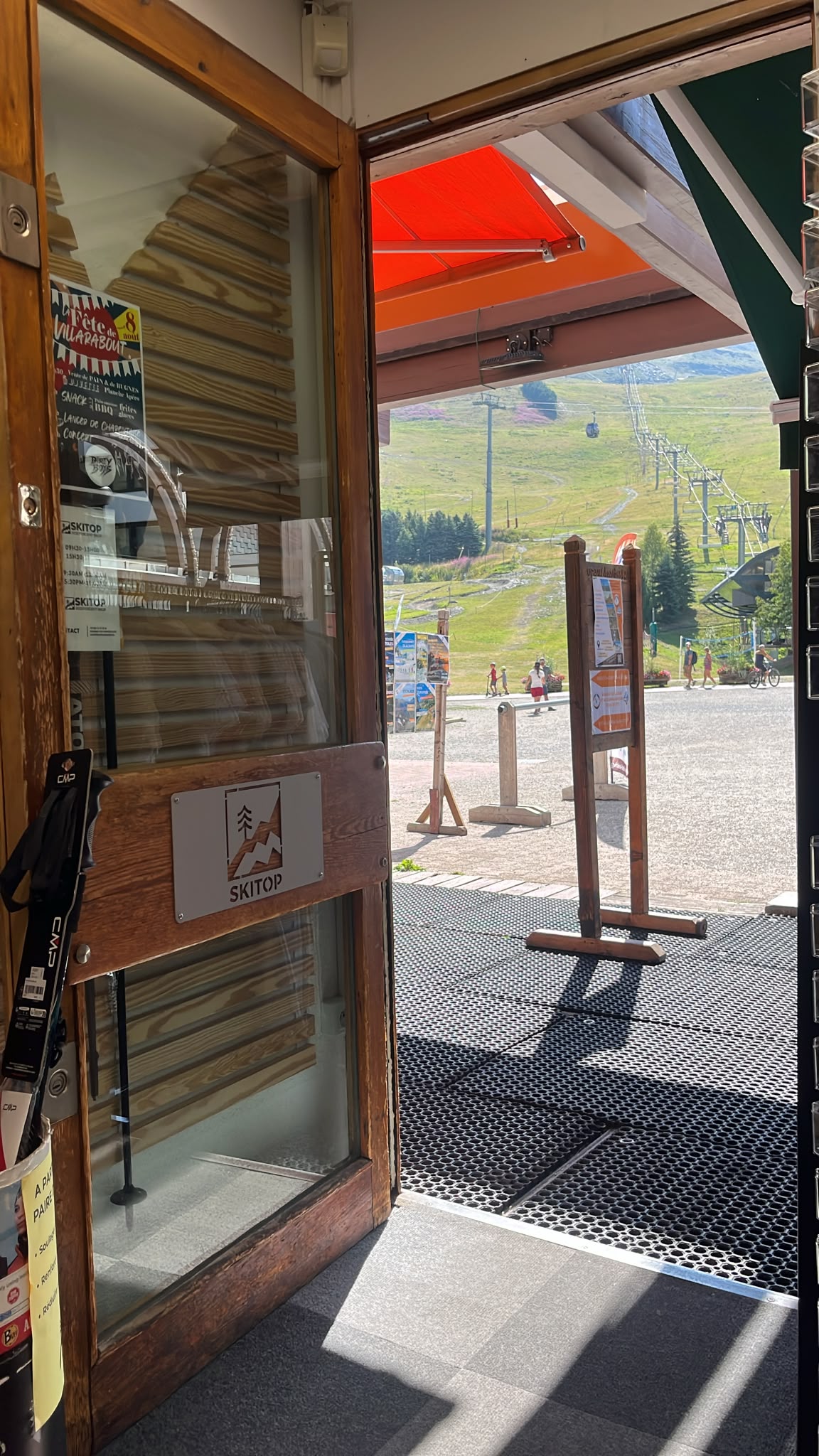 Entrance to the SKITOP rental shop opening onto a green mountain resort with its ski lifts in summer.